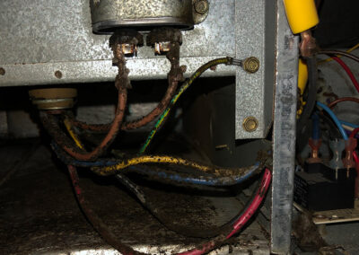 Close-up of corroded electrical wires inside a HVAC system, showing rust buildup on components and dirty, disorganized wiring.