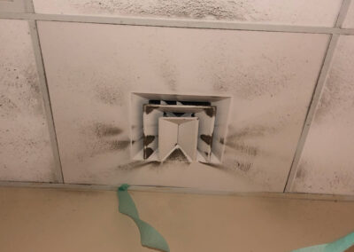 Dirty ceiling air vent surrounded by dust and dark stains, with visible buildup on the vent blades and nearby ceiling tiles.