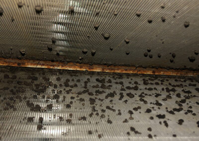 A close-up of a contaminated HVAC coil covered with a substantial buildup of dirt, debris, and mold-like spots.