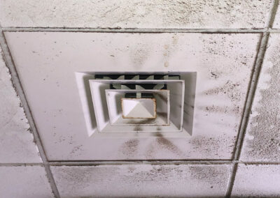 A vent cover and surrounding ceiling tiles are heavily soiled with black dust, indicating poor air quality and lack of cleaning maintenance.