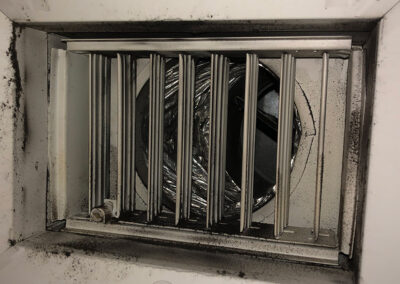 A close-up view of a heavily soiled air vent, coated with dirt and grime, with vent slats coated in black dust.