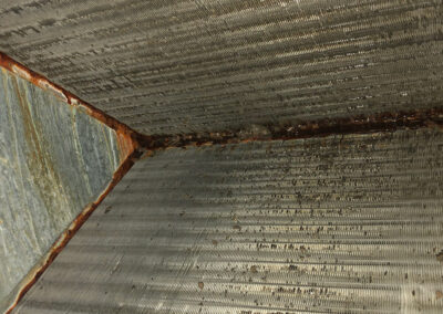 Close-up of dirty, rust-covered metal fins inside an HVAC system, showing significant corrosion and grime buildup along the edges.