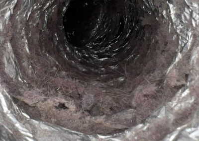 Close-up shot of a dryer vent filled with lint, dust, and debris inside, obstructing airflow.