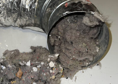 A disconnected dryer vent hose showing significant lint buildup around the vent opening.