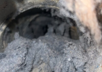 A severely clogged dryer vent, packed with thick layers of lint and debris that are obstructing airflow and increasing fire risk.