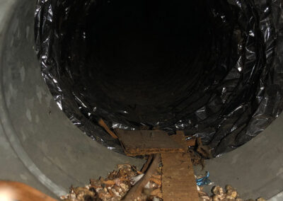 Air duct filled with debris, including wood, leaves, and dirt, obstructing the airflow and indicating poor air quality.